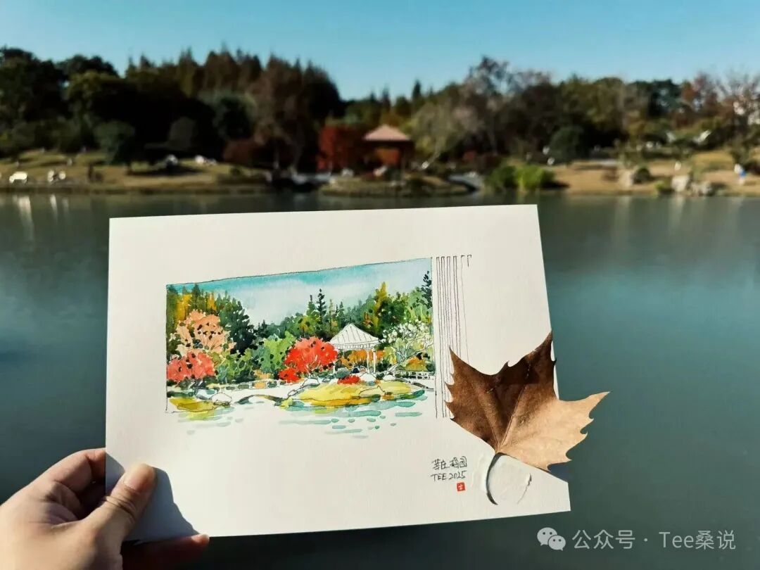 手持湖边亭子与树林的水彩写生，背景是现场湖景